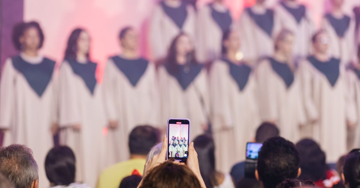 A diverse group of young Ghanaians gathered in a modern church auditorium, smiling and holding smartphones, with a stage in the background