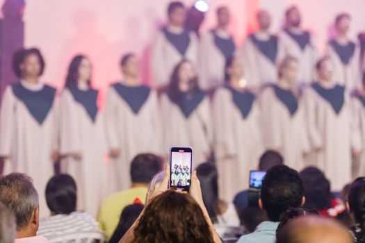 An audience records a live choir performance with smartphones indoors.