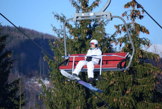 A snowboarder in winter sportswear enjoys a scenic ascent on a ski lift surrounded by snow-dusted trees.