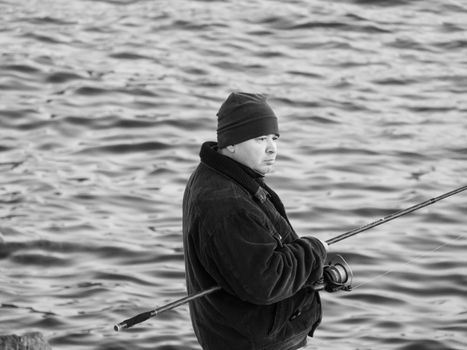 A serene black and white image capturing a fisherman with a rod overlooking the water.
