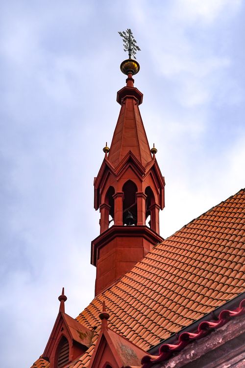 Free Low angle shot of a Gothic-style church bell tower with intricate red architectural details against a clear blue sky. Stock Photo