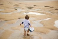 一个孩子提着水桶，在阳光明媚的日子里沿着沙滩散步，享受休闲时光