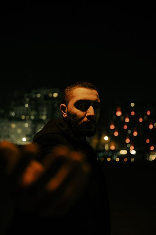 Free A dramatic portrait of a man reaching out in a dimly lit urban setting at night. Stock Photo