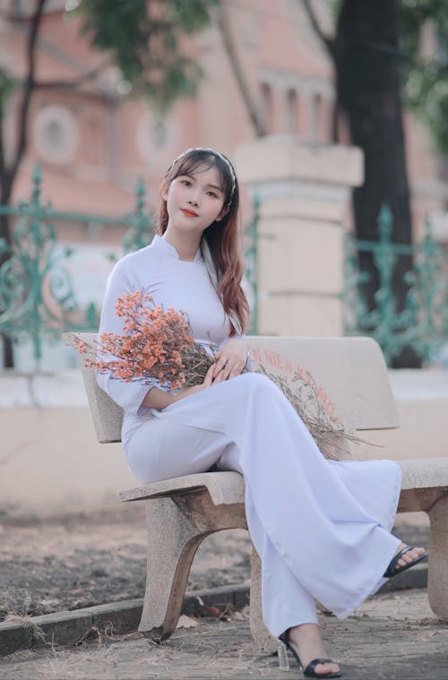 Free Woman Holding Flowers While Sitting on a Bench Stock Photo