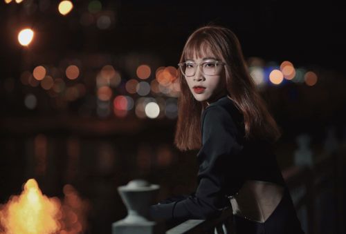 Free Elegant portrait of a woman with eyeglasses and black attire standing by a railing at night. Stock Photo