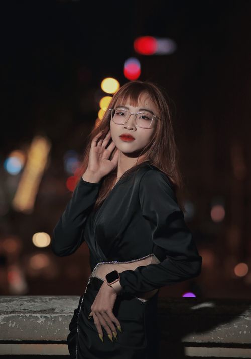 Free Beautiful woman posing confidently in a stylish black dress with bokeh lights at night. Stock Photo