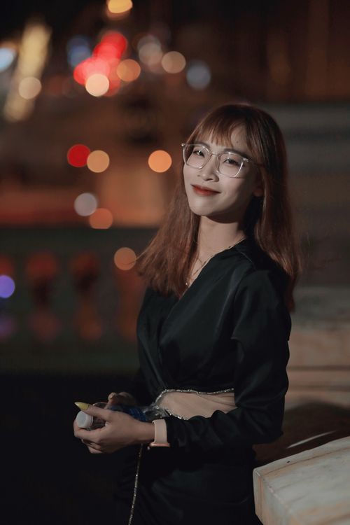 Free Smiling Asian woman in a black dress, captured with bokeh lights at night, creating a vibrant and warm ambiance. Stock Photo