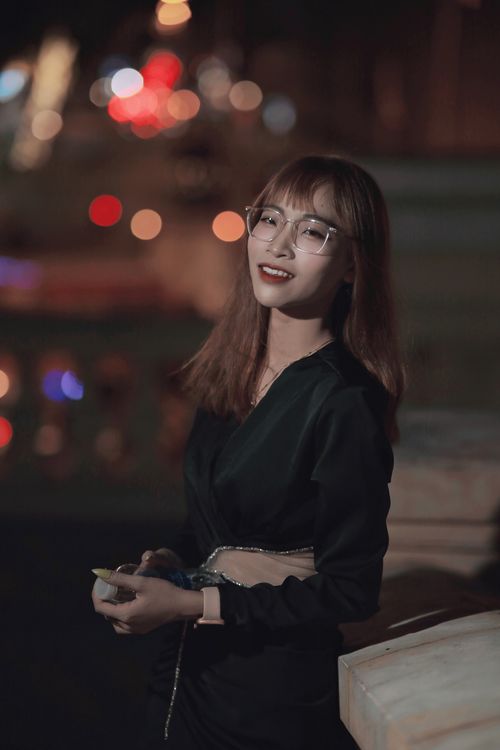 Free A smiling woman in a black dress poses at night with vibrant bokeh lights in the background. Stock Photo