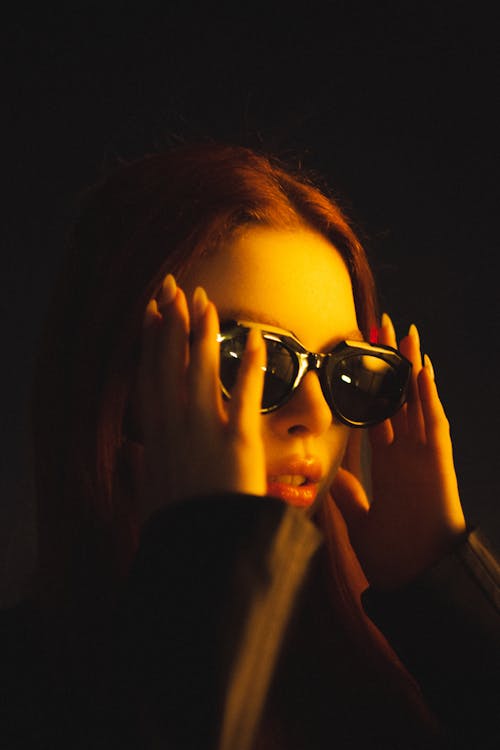 Photo of a Woman Wearing Sunglasses with Hands Raised on Head