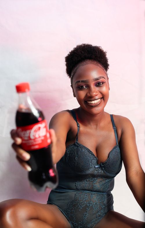 Free African woman in lingerie smiles holding a soda bottle, blending fashion and lifestyle photography. Stock Photo