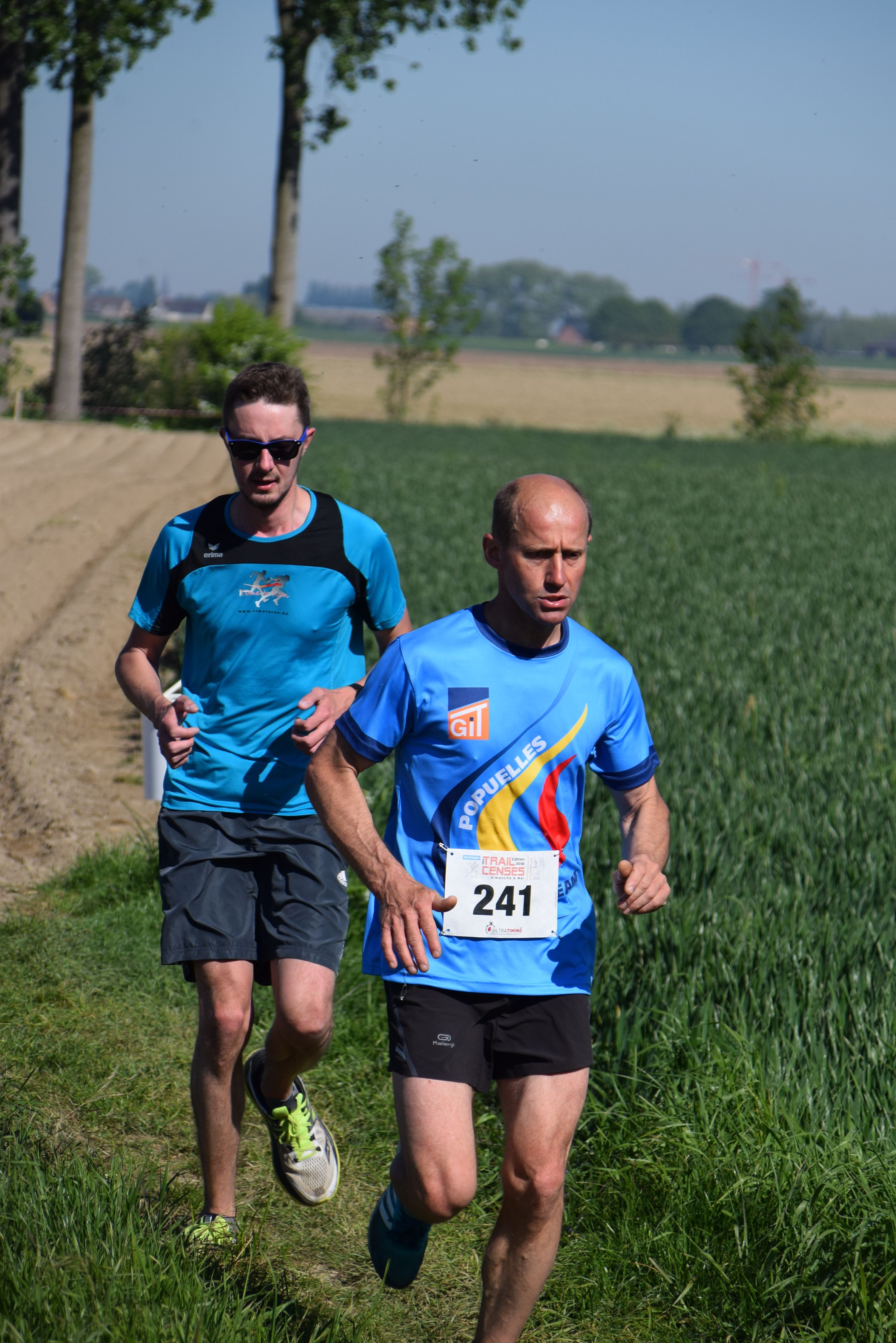 Dos corredores adultos con dorsales compitiendo en una carrera por el campo