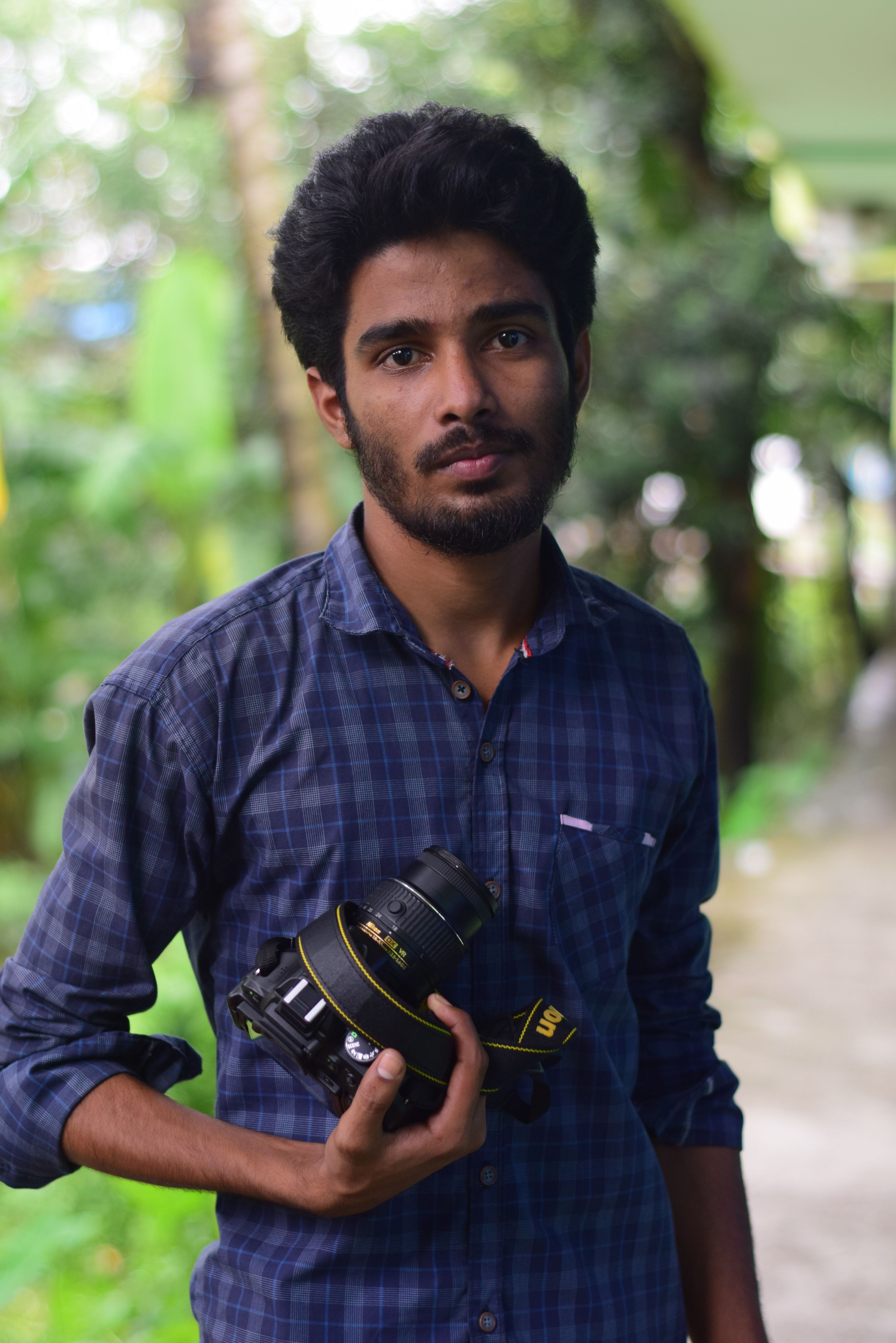 Stylish man with a beard holding a DSLR camera outdoors. Casual and natural look.