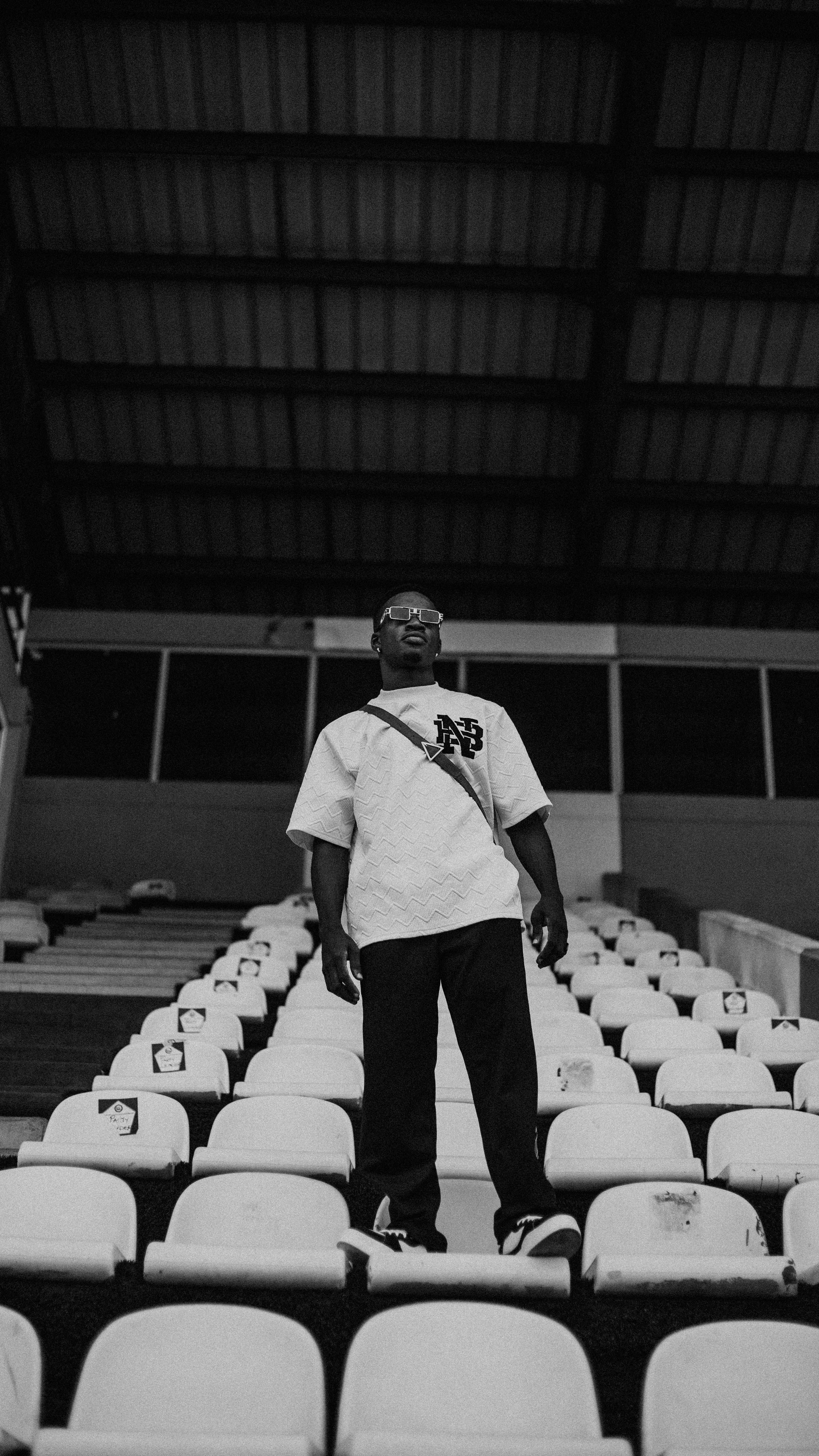 A solitary man stands in a stadium, captured in black and white, exuding a contemplative ambiance.