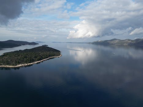 Serene aerial shot of Mali Iž island reflecting on the Adriatic Sea with a cloudy sky.