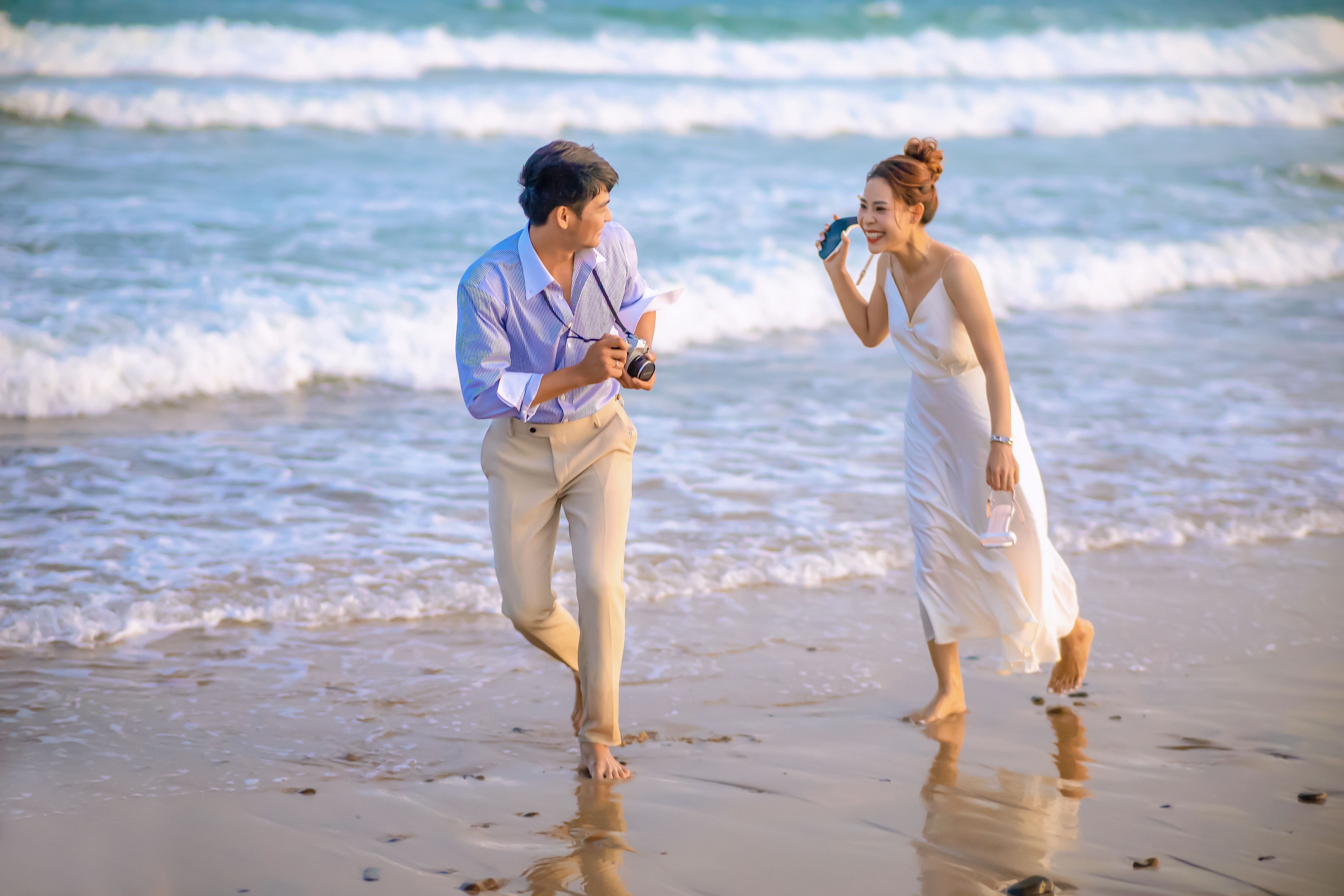 A joyful Asian couple shares a romantic moment while walking along a sunny beach.