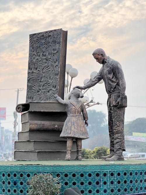 Statue of a Little Girl and a Man next to Large Books 