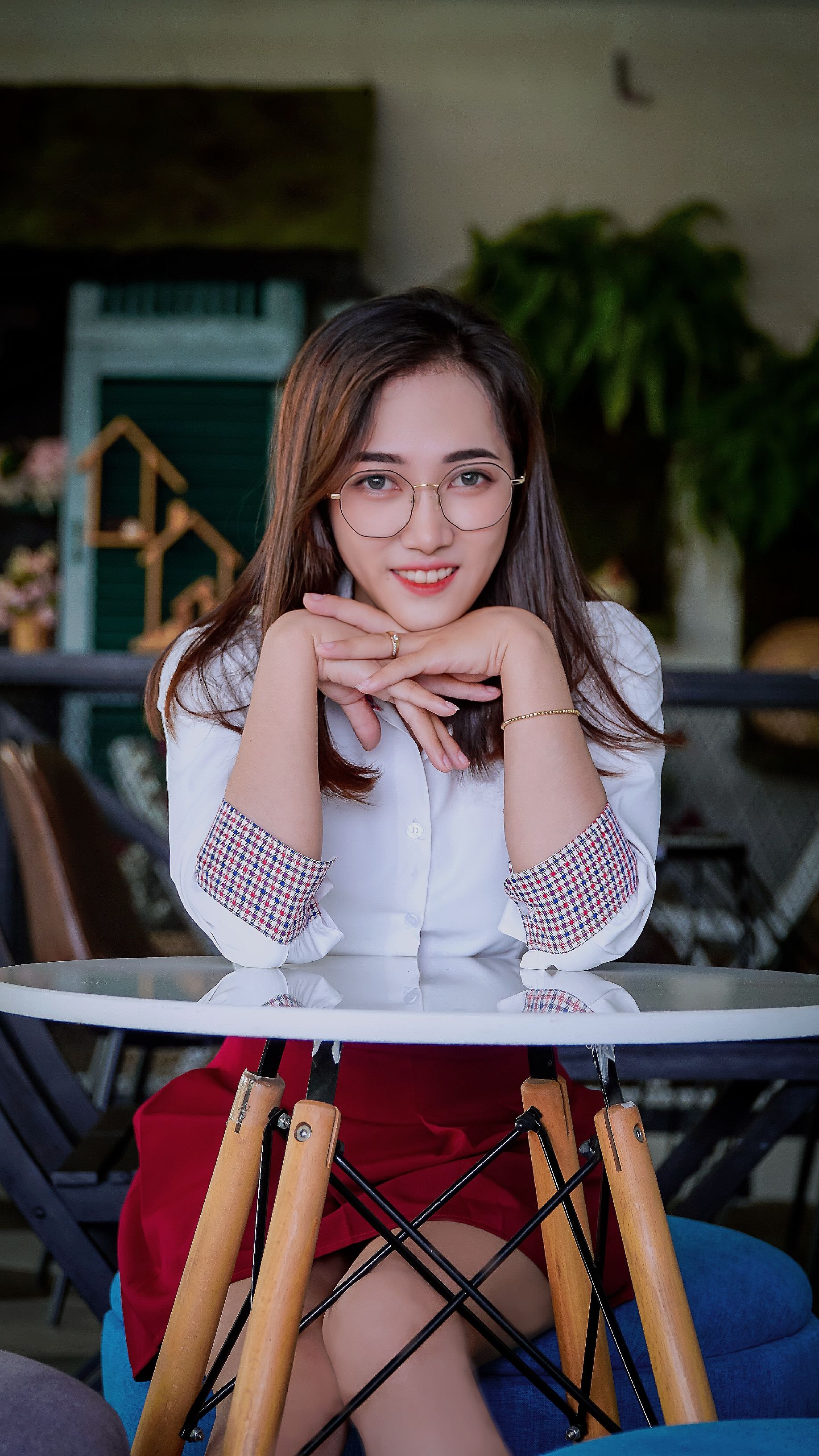 Charming Asian woman with glasses, smiling confidently while seated at a table indoors.