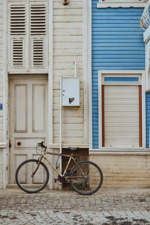 Free A classic bicycle leans against a rustic wooden facade with blue accents, creating a nostalgic street scene. Stock Photo
