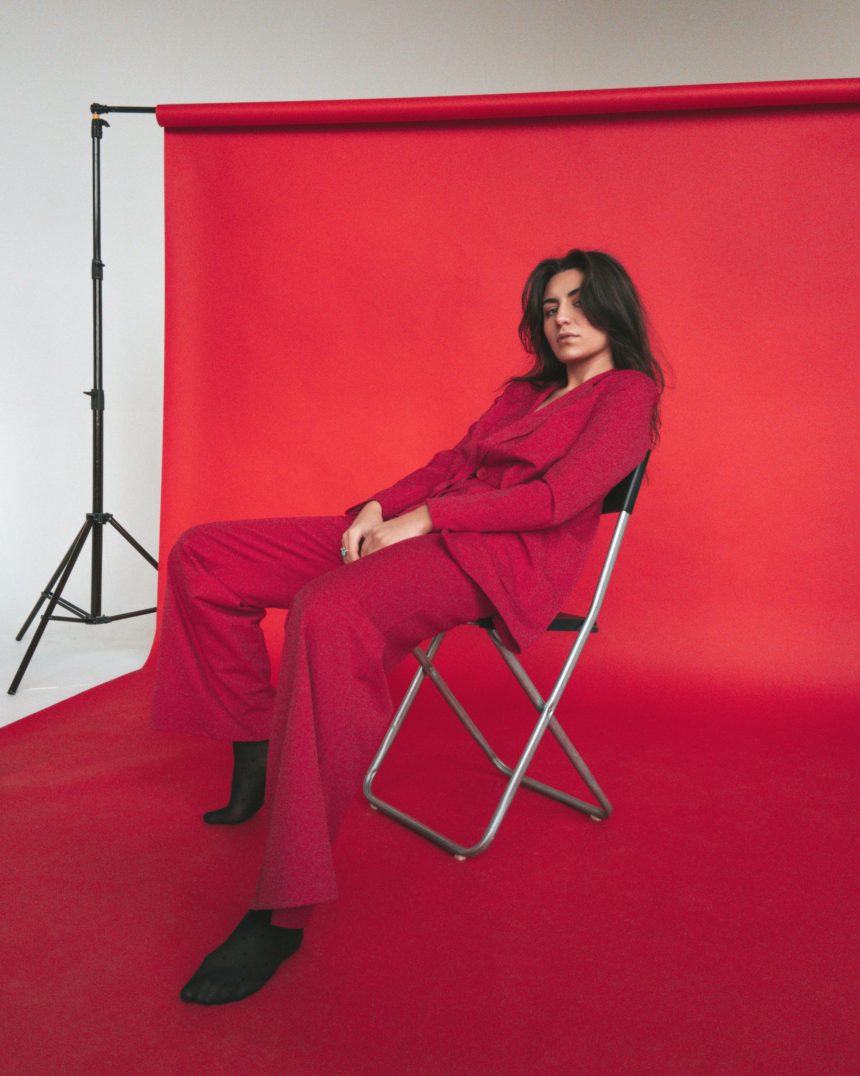 一位穿着红色服装的时尚女性在现代工作室的椅子上摆姿势