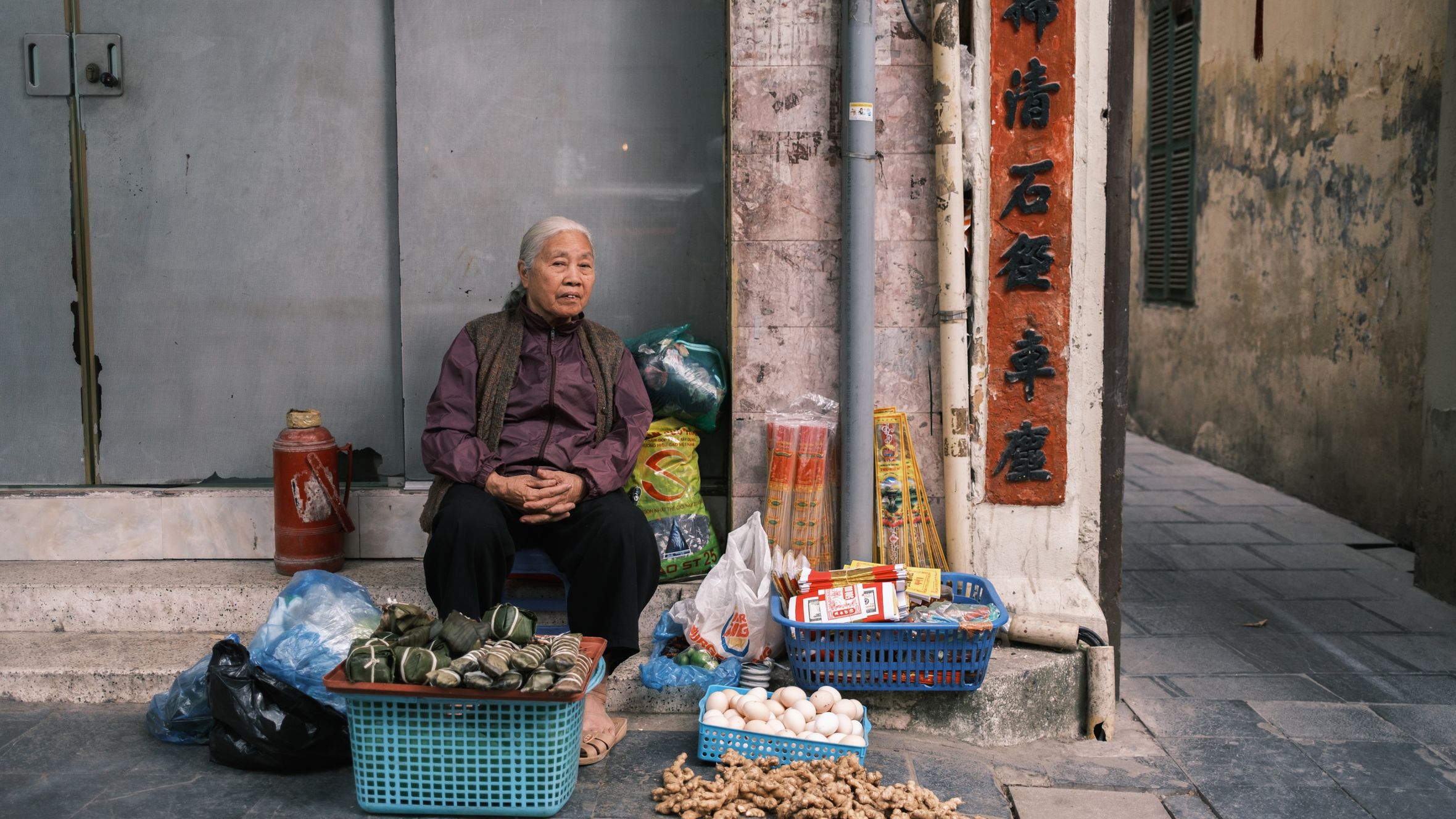 Elderly woman selling fresh produce on a city street, showcasing local culture.