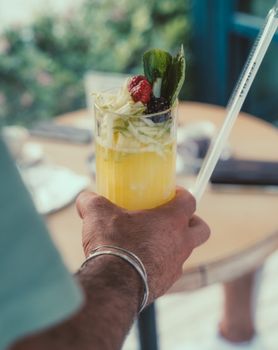 A vibrant cocktail with fruits and herbs in a hand-held glass, perfect for summer.