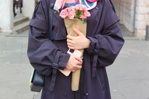 Free A woman in a dark coat holds a bouquet of pink flowers outdoors on a city street. Stock Photo