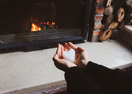 Hands Holding Snow Heart near Fireplace