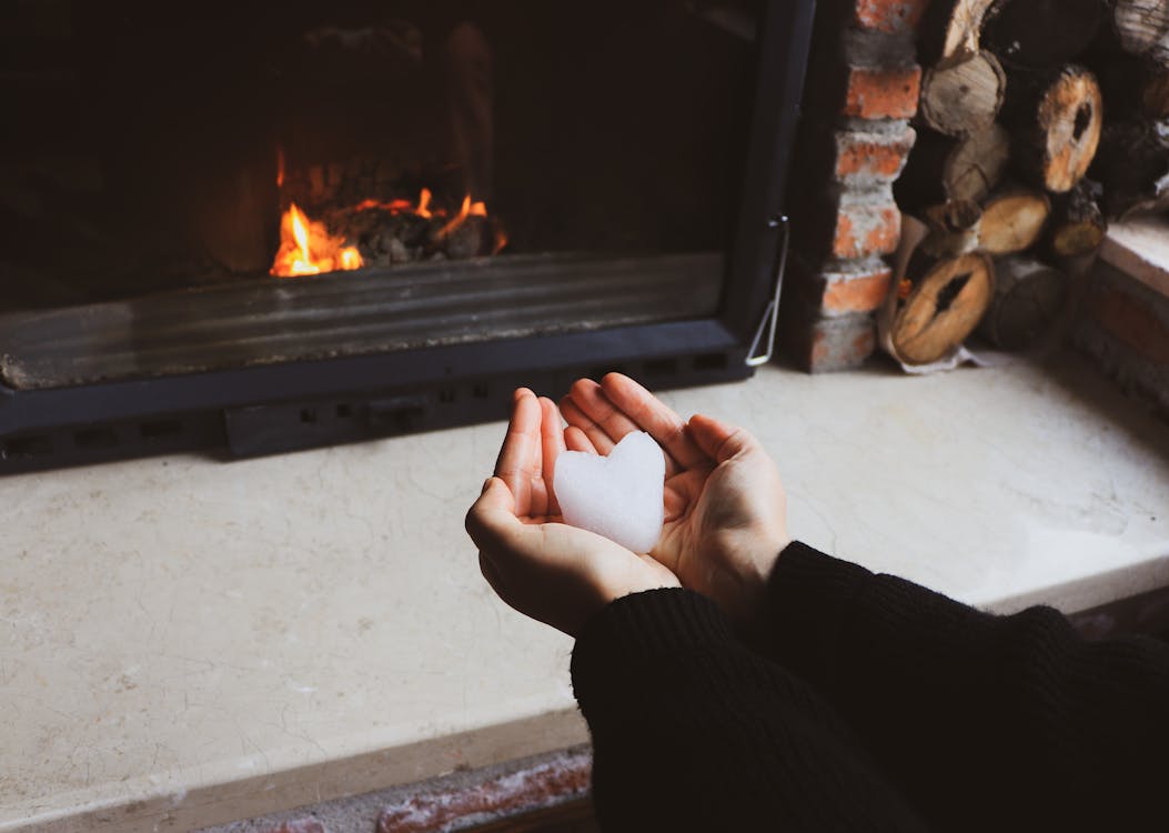 Hands holding a snow heart in front of a fireplace