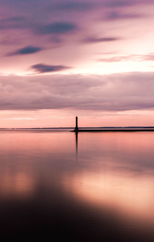 Free Peaceful sunset over the ocean with tranquil reflections and a silhouette on the horizon. Stock Photo