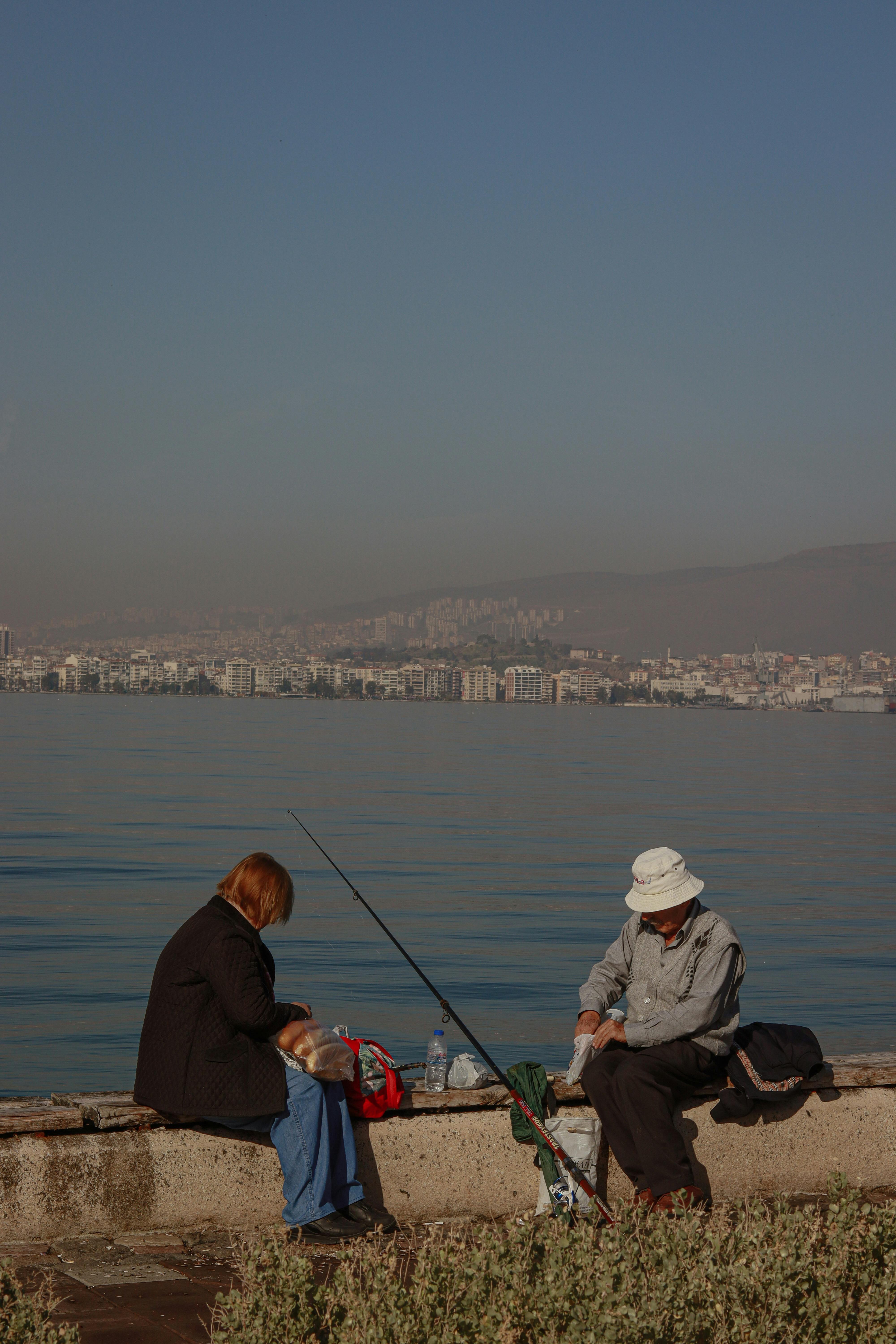 two people sitting on a bench by the water