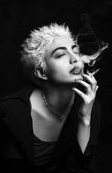 A dramatic black and white portrait of a woman smoking with eyes closed.