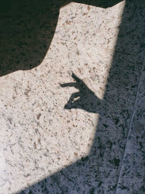 Shadow of a hand forming a gesture on a textured granite floor in sunlight.