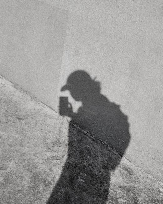 Silhouette of a person with a smartphone casting a shadow on a concrete wall.