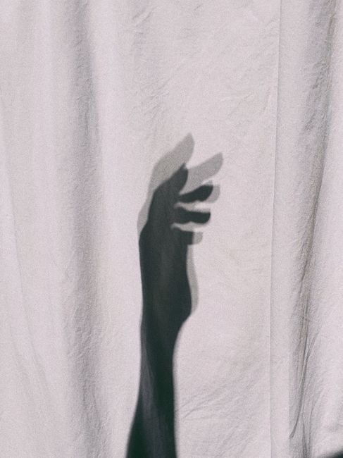 A creative grayscale image showing the shadow of a hand on textured fabric, abstract and minimalist.
