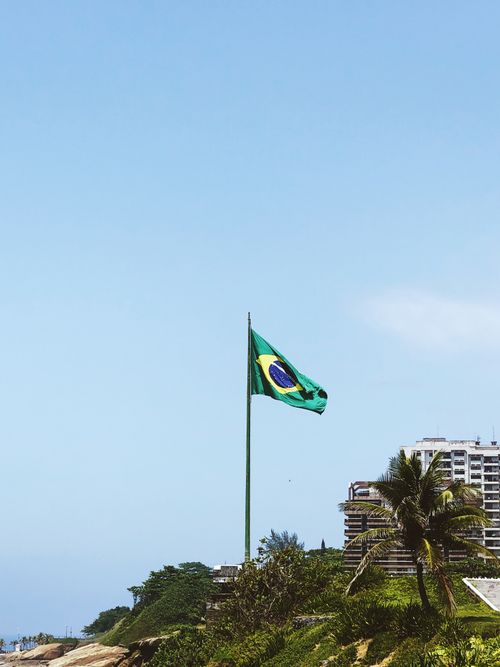 Free A Brazilian flag on a flagpole by the coastline with urban buildings in Rio de Janeiro. Stock Photo
