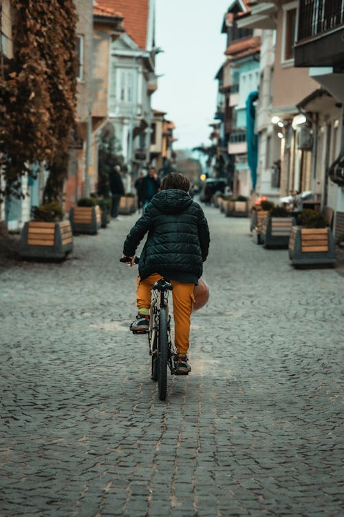A Boy in a Puffer Jacket Riding a Bike on a Cobblestone Street