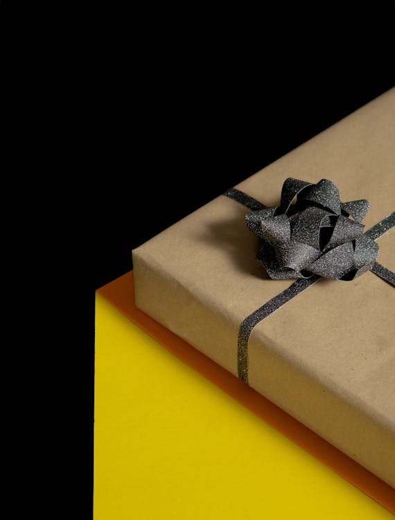 Craft paper gift box with a shimmering black bow on a yellow background.