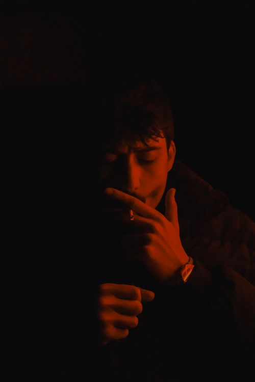 Free Dramatic low-light portrait of a man smoking in the dark, creating a mysterious mood. Stock Photo