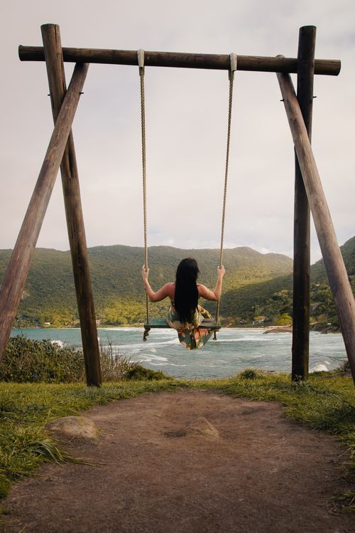 Free A woman on a swing enjoys a tranquil landscape overlooking a river and hills. Stock Photo