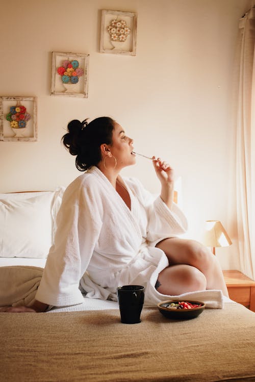 Woman in a White robe having a fondue on the bed in front of window