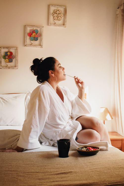Breakfast In Robe Woman in a White robe having a fondue on the bed in front of window ...