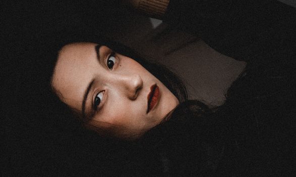 A close-up portrait of a woman with red lipstick, captured in soft and moody lighting.