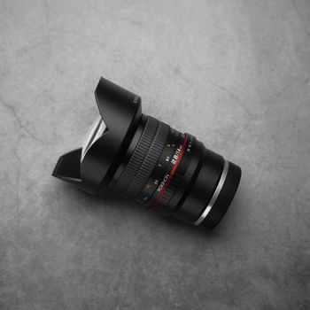 A detailed close-up shot of a black camera lens placed on a textured gray background.
