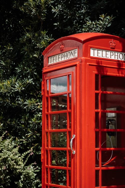 Free Iconic red British telephone booth surrounded by greenery on a sunny day. Stock Photo