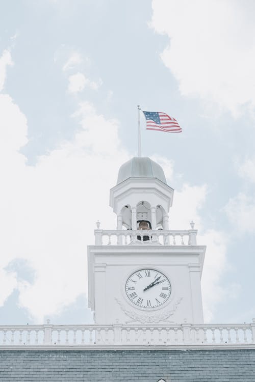 Low Angle Shot of a Clock Tower with Waving American Flag 