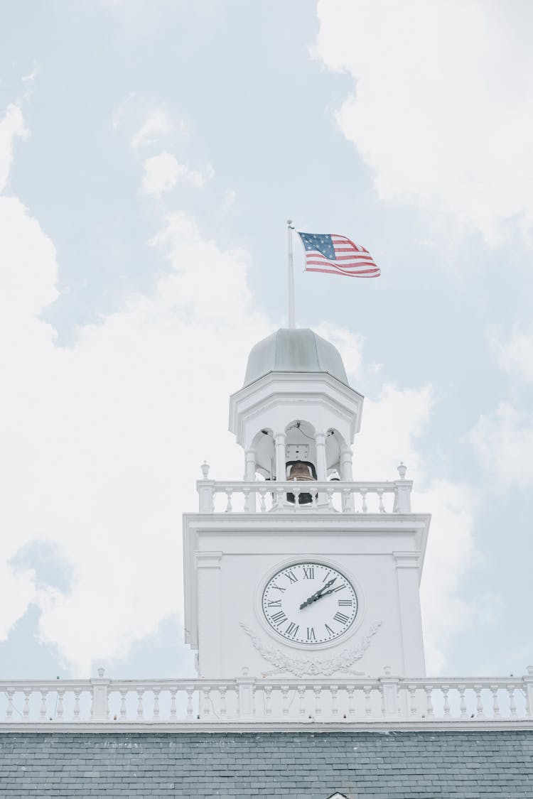 Low Angle Shot Of A Clock Tower With Waving American Flag 