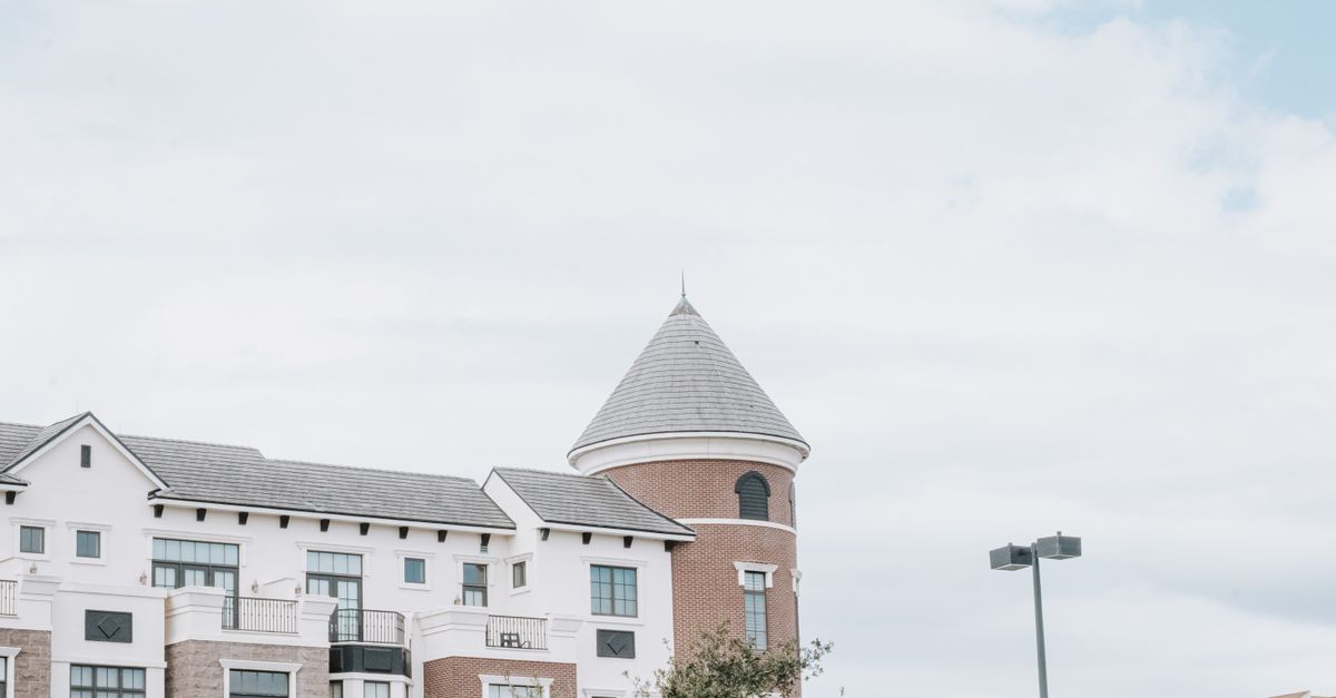 A stylish urban residential building featuring red brick and modern architectural design with a tower.
