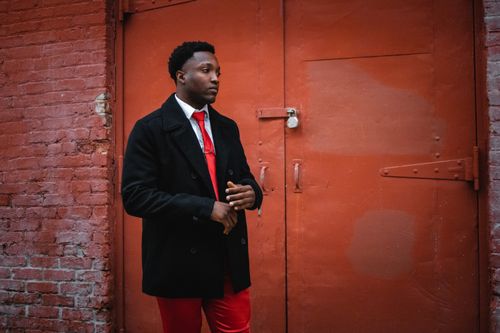 Free Stylish man in a black coat posing against a rustic red brick wall and door. Stock Photo