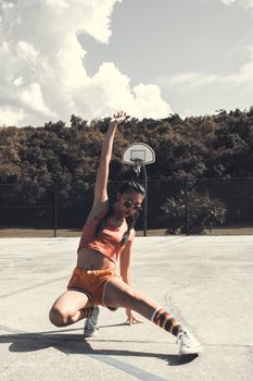 Woman performing break-dancing on an outdoor basketball court in summer, showcasing athleticism.