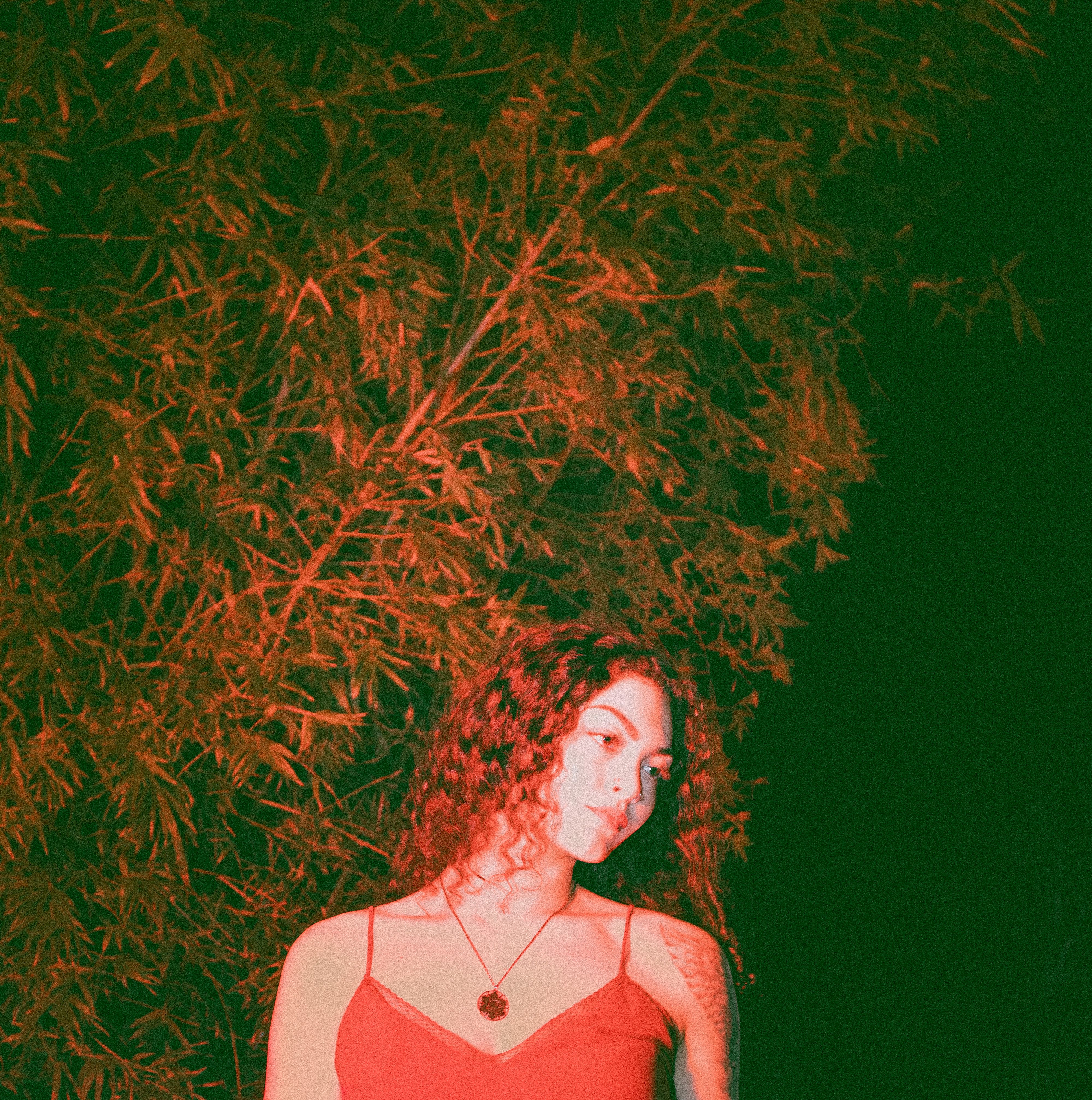 A young woman with curly hair poses elegantly outdoors at night with creative lighting.